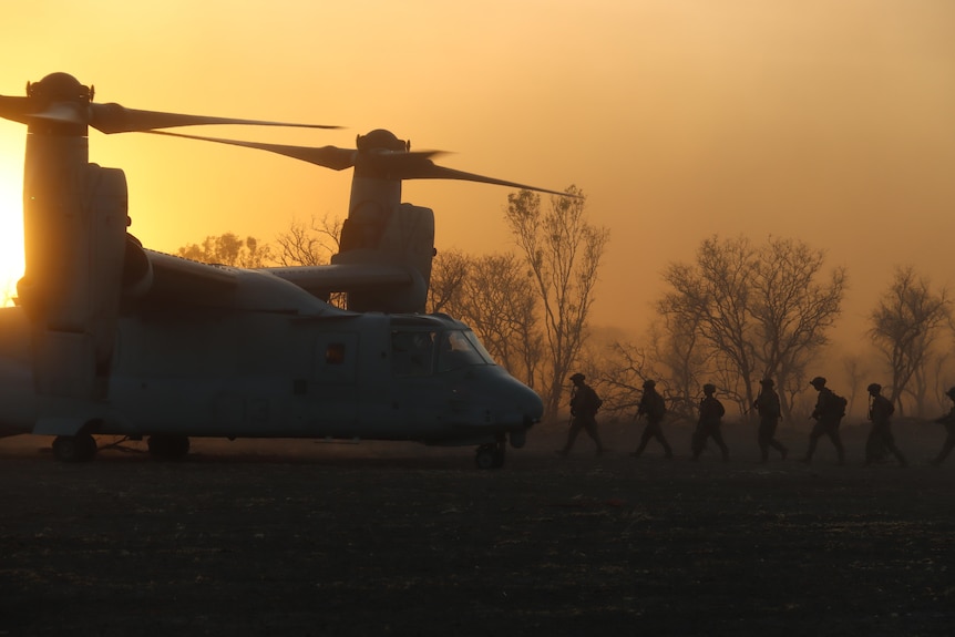 Marines line up in single file to enter a plane at dusk
