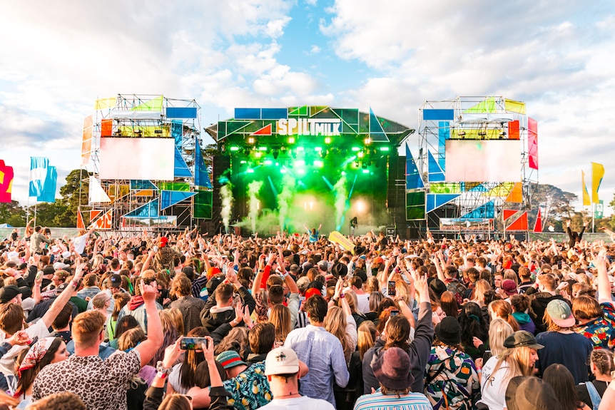 A crowd of people face a brightly lit stage with the words 'Spilt Milk' atop it.