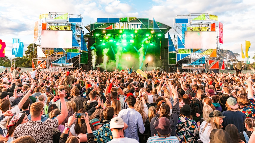 A crowd of people face a brightly lit stage with the words 'Spilt Milk' atop it.