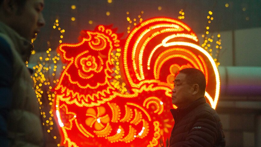 Man walks past rooster neon sign in Beijing