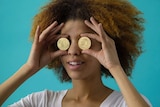A woman holding up two gold coins to her eyes.