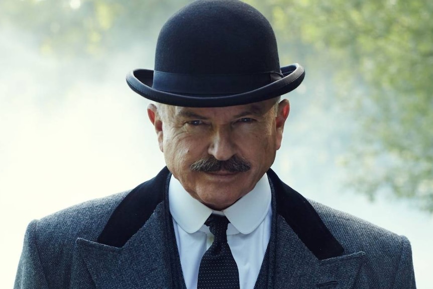 A bespectacled Sam Neill in a bowler hat, and suit