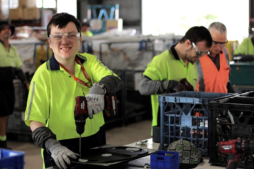 A young man wearing a high visibility shirt uses a drill in a workshop