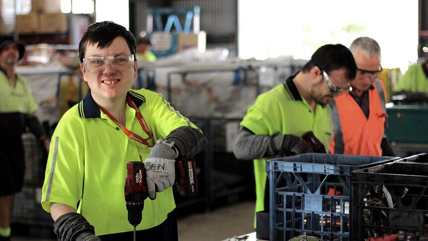 A young man wearing a high visibility shirt uses a drill in a workshop