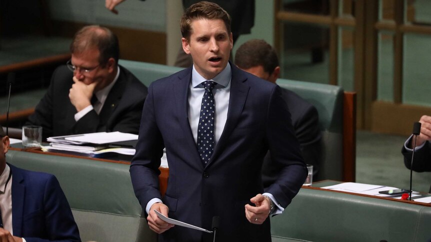 Andrew Hastie stands up in the House of Representatives with a piece of paper in hand.