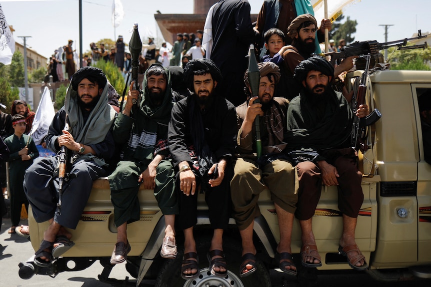 Taliban members are seen holding guns on the back of a truck. 