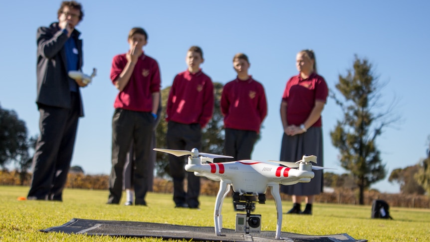 A drone on the ground with students and instructor standing in the background.