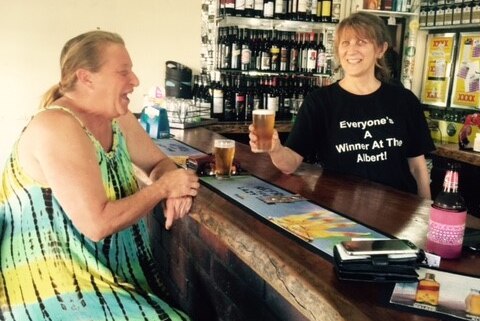 Dianne Falzon holding up a beer with a patron on the other side of the bar.
