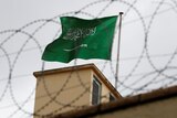 Saudi Arabia's flag flies behind a fence topped with barbed wire.