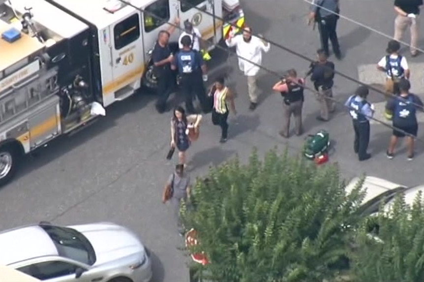 An aerial shot shows people walking, some with their hands in the air, past authorities.