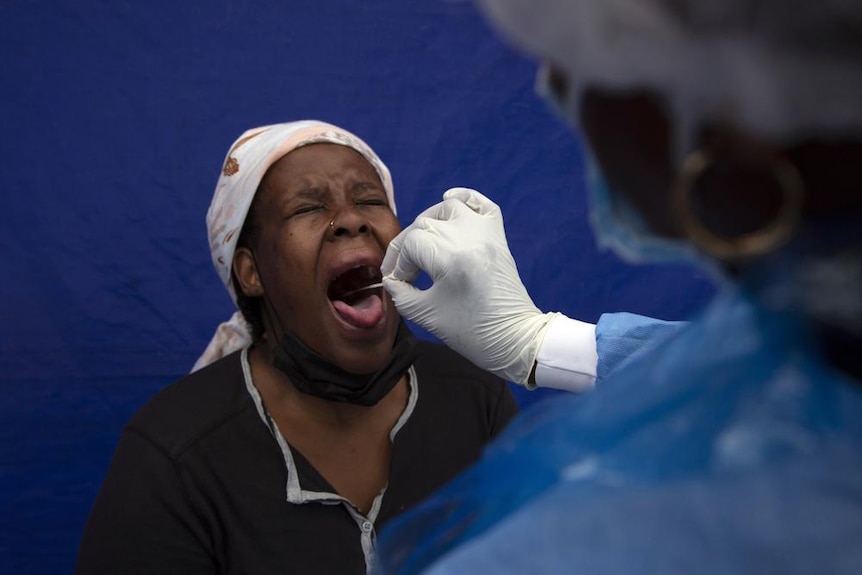 O femeie scoate limba pentru a lua un tampon din gura unei persoane care poartă haine de protecție 