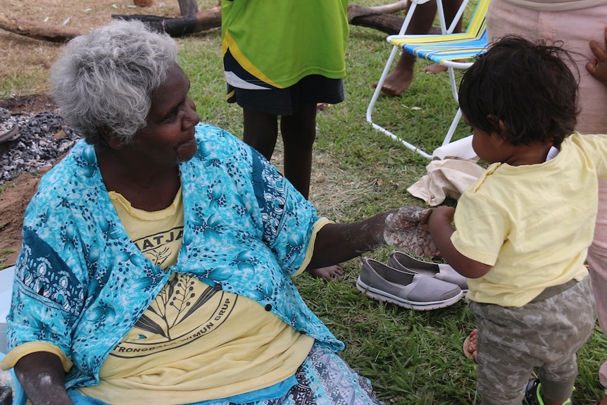 Jocelyn McCartney shakes hands with a small boy as she sits on the grass