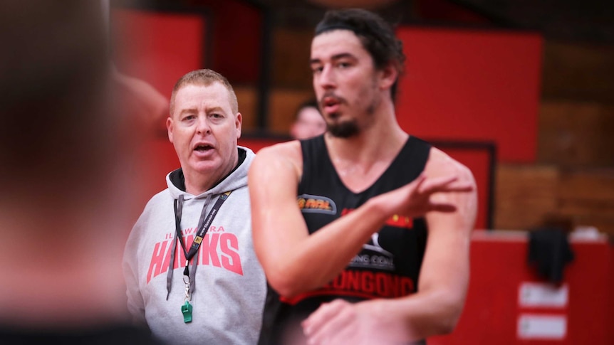 A basketball coach watches on while players train.
