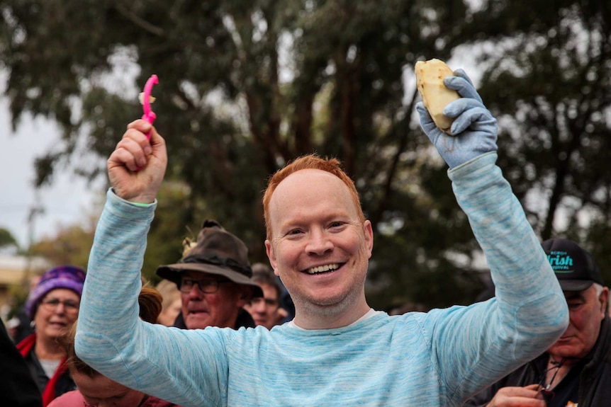 A man with red hair holding a peeled potato in the air