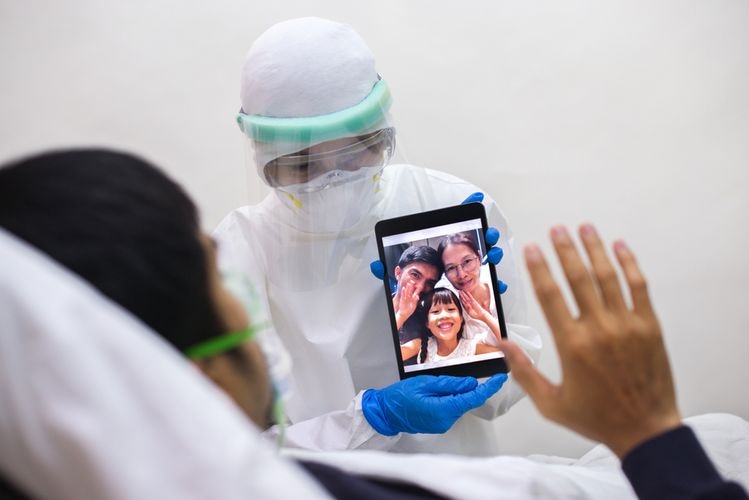 A medic shows a patient an ipad displaying an image of a waving family.