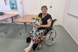 A lady with a broken leg sits in a wheelchair holding flowers