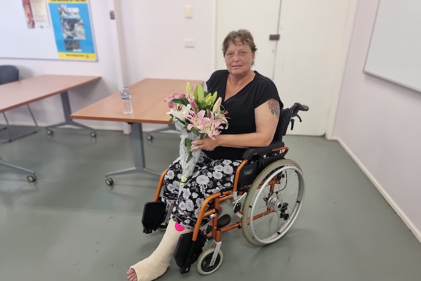 A lady with a broken leg sits in a wheelchair holding flowers