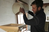 a farmer pour spelt wheat into a small hopper made from pine