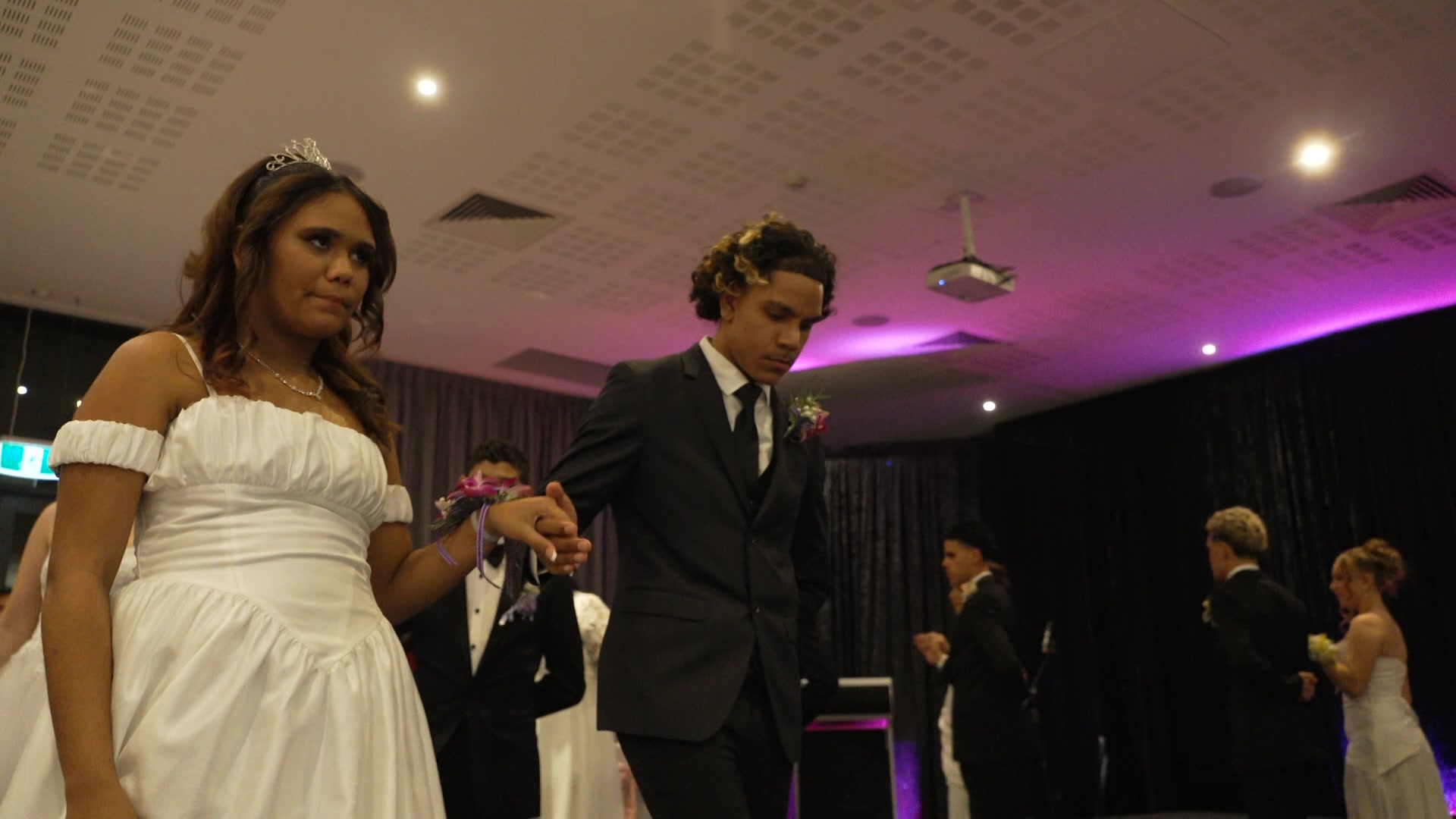 a young couple, dressed in a black suit and a white dress hold hands