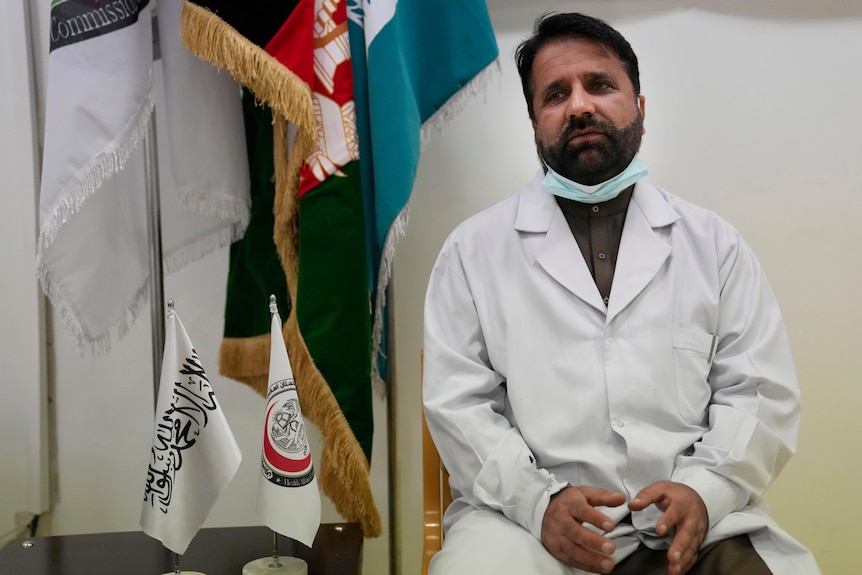 Doctor in a white coat with flags in the background of his office looks sad.