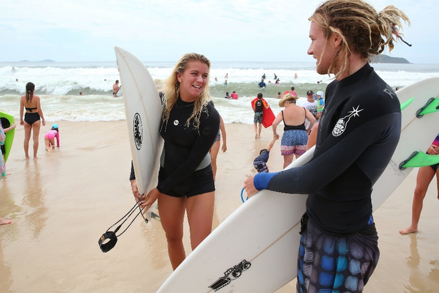 A woman can be seen holding a surfboard on a crowded beach.