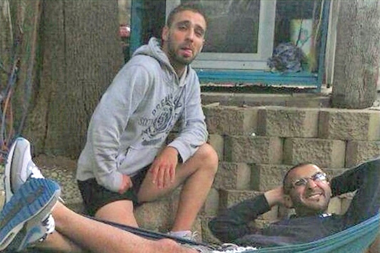 Omar Al-Kutobi kneels next to Mohammad Kiad as he lies in a hammock