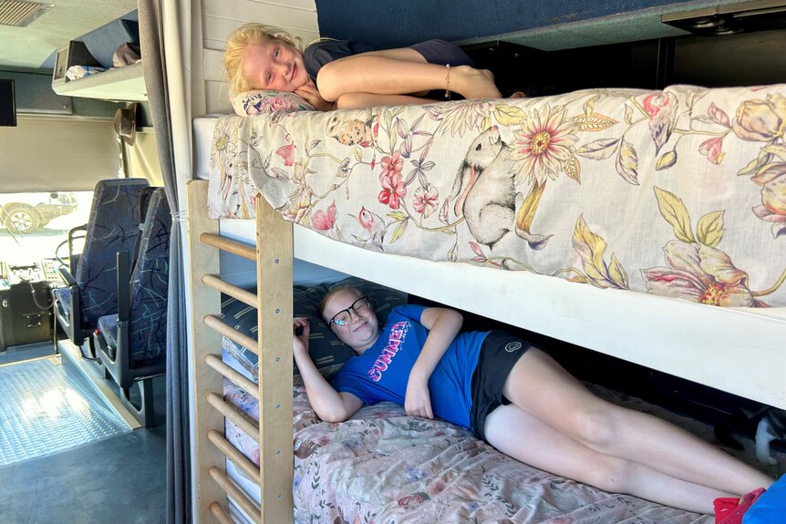 Two young children lie on bunk beds inside a bus. 