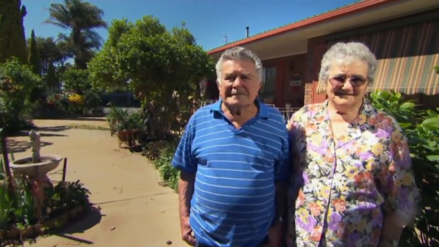 Elderly couple stand outside their house