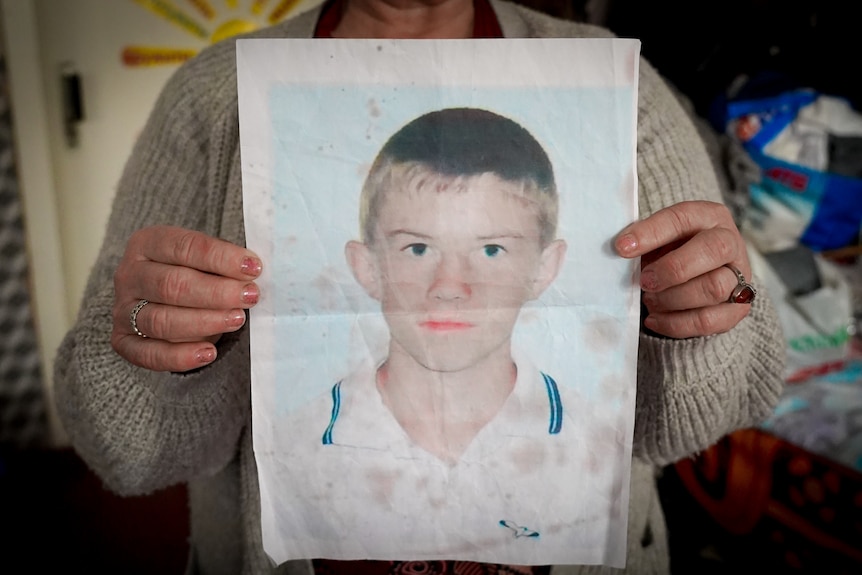 A woman's hands hold a large printout of a young man's passport photo