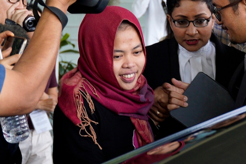 A woman in Islamic headdress smiles as she leaves a court while surrounded by lawyers and media.