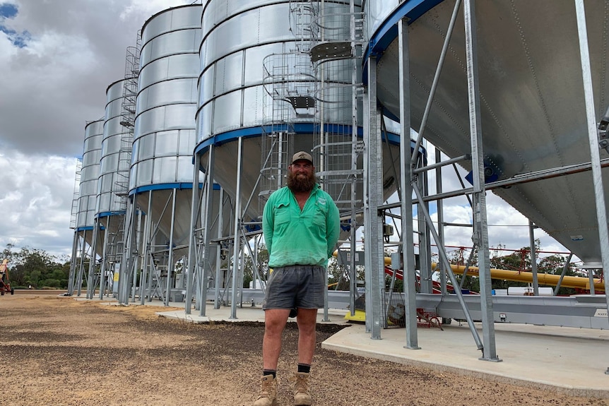A man in a green shirt stands in front of silos