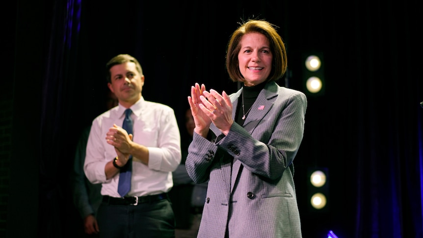 Catherine Cortez Masto smiles and claps on a stage with lights behind her