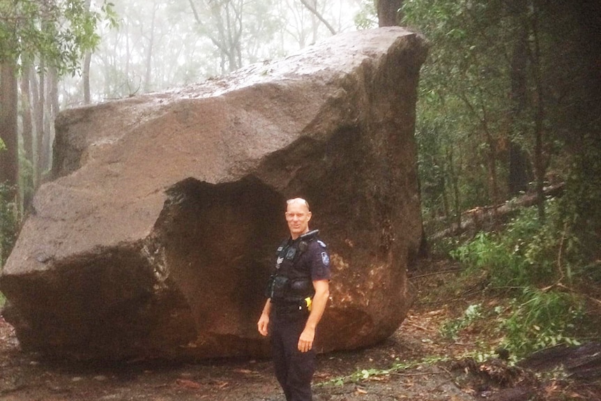 Police officer stands inf front of huge rock that fell onto Tamborine Mountain Road at Mount Tamborine in a serious landslide.
