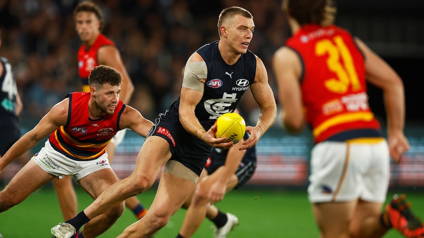 Carlton's Patrick Cripps turns his body in mid-run as he prepares to handball while Crows defenders try to run at him.