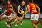 Carlton's Patrick Cripps turns his body in mid-run as he prepares to handball while Crows defenders try to run at him.