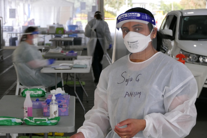a woman in full PPE at a COVID-19 testing site looks at the camera