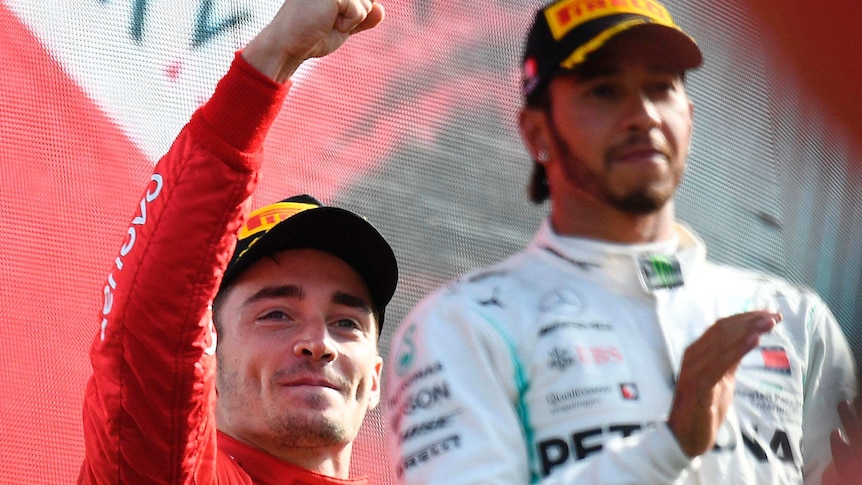 Charles Leclerc celebrates with a raised fist standing in front of and to the left of Lewis Hamilton who is clapping