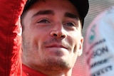 Charles Leclerc celebrates with a raised fist standing in front of and to the left of Lewis Hamilton who is clapping