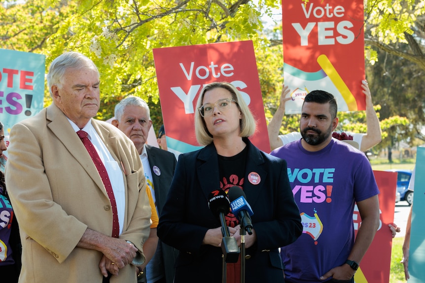 Kim Beazley wears a brown jacket and stands next to Hannah who speaks at a Yes rally for the Voice to Parliament