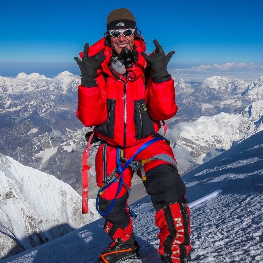 A man in a red snow suit standing on a snowy peak