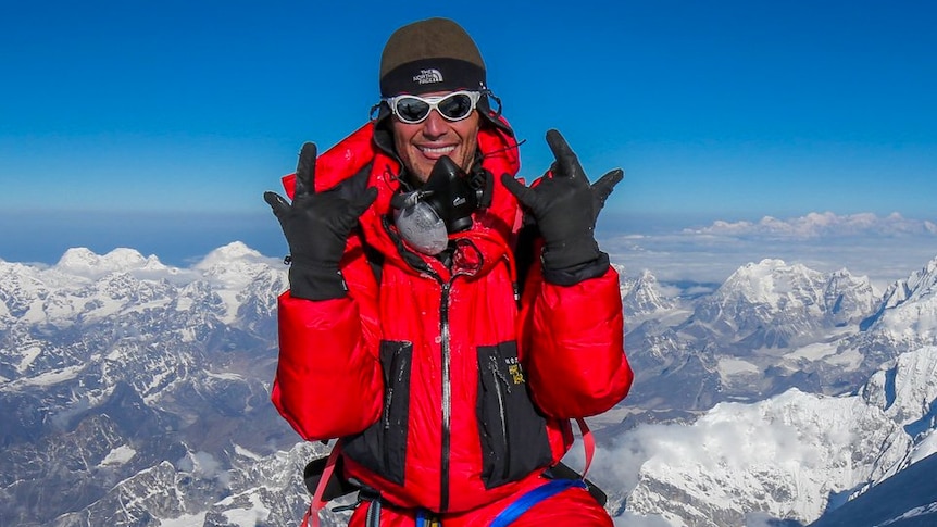 A man in a red snow suit standing on a snowy peak