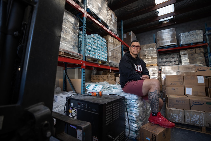 Dave sits on a crate of food supplies in the middle of a warehouse