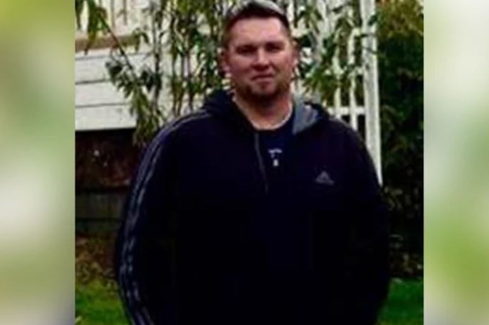 An amateur photo of a man in a navy tracksuit standing in a garden.