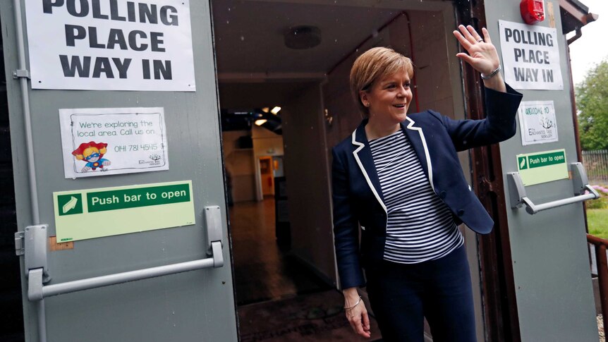 Nicola Sturgeon, First Minister of Scotland, waves after voting in Glasgow walking by a black and white polling sign.