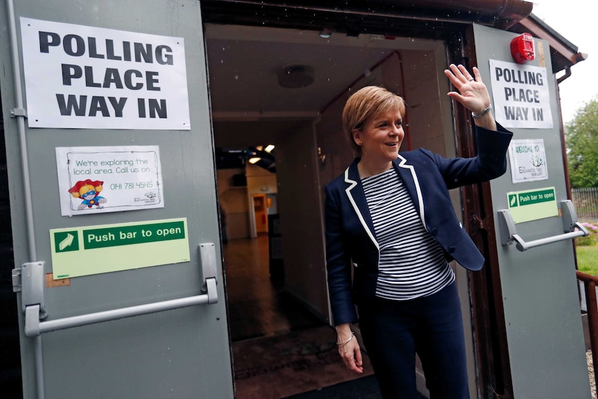 Nicola Sturgeon, First Minister of Scotland, waves after voting in Glasgow walking by a black and white polling sign.