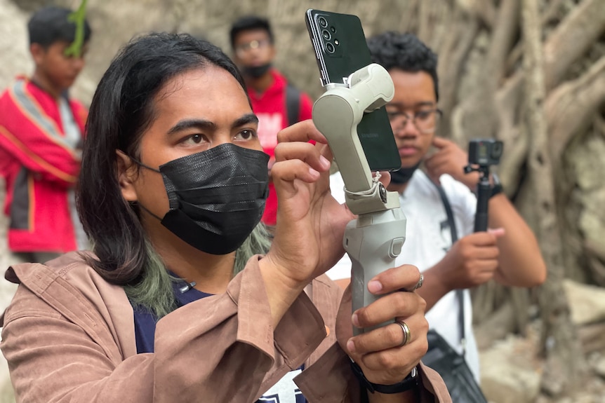 A man holds a mobile phone on a handle.