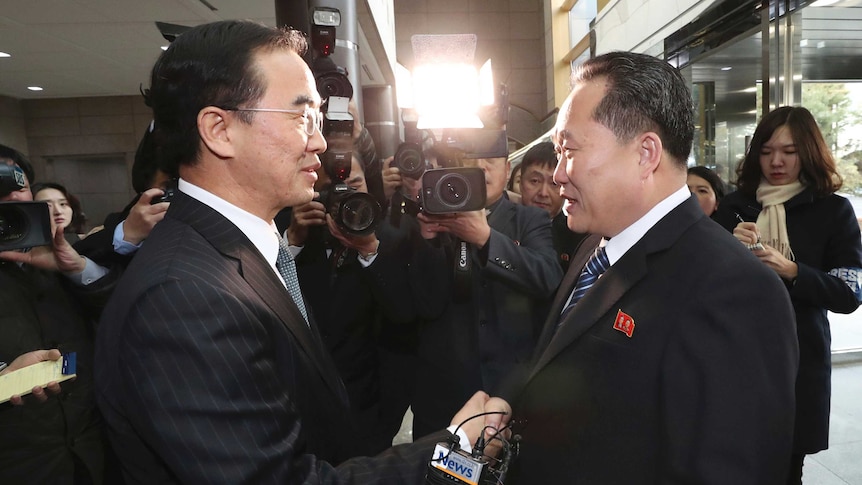 South Korea's Cho Myoung-gyon and the North's Ri Son Gwon shake hands and smile in front of cameras and reporters.