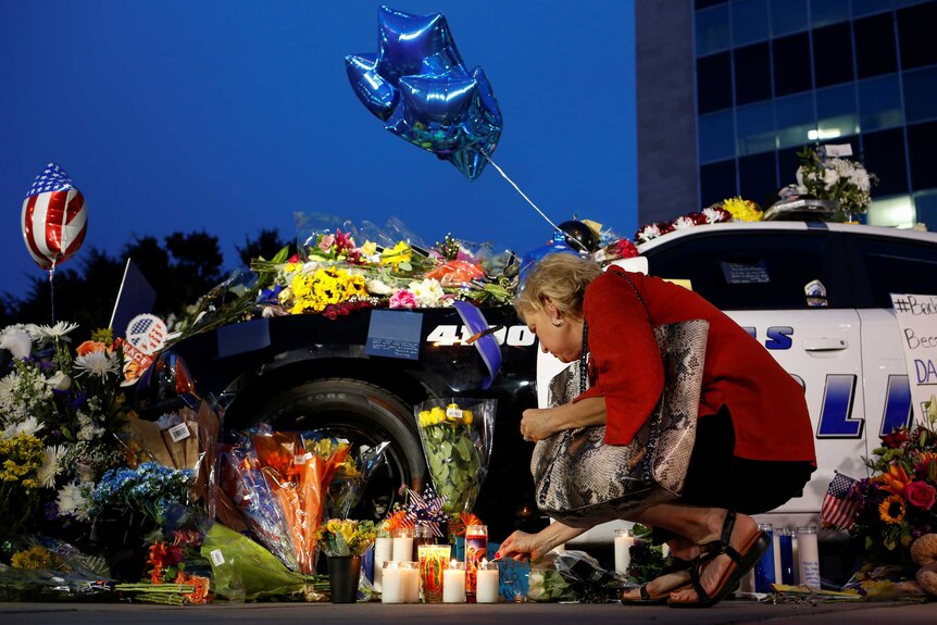 A woman lights a candle at a makeshift memorial featuring flowers on a Dallas Police car.