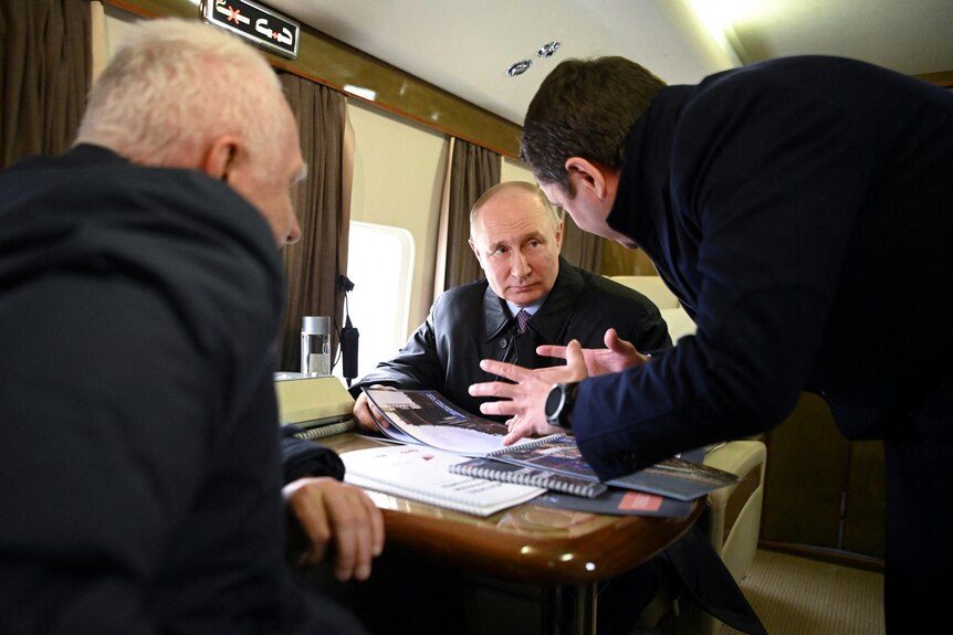 Putin next to a man with open hands on a plane 