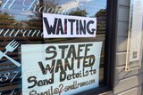 A sign saying 'staff wanted' in the window of a restaurant.